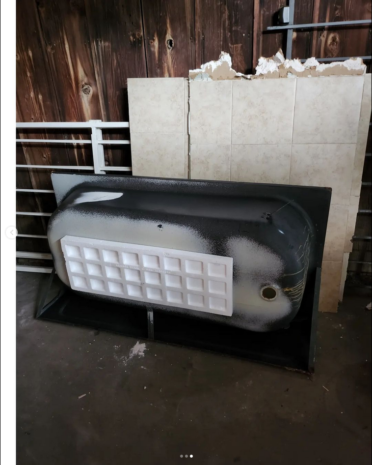 image shows an uninstalled bathtub laying on it's side. Behind the bathtub are sections of tile wall that has also been removed.